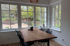 Ein Essbereich mit einem Holztisch und Stühlen, große Fenster mit Blick auf einen Garten und ein Gebäude.