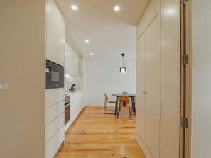 Een moderne keuken met witte kasten, een ingebouwde oven en een eethoek met een ronde tafel en twee stoelen.