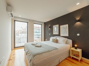 Ein modernes Schlafzimmer mit einem großen Bett, einem Nachttisch mit Lampe und Blick auf die Stadt durch ein großes Fenster.