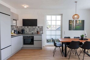 A modern kitchen with a dining area, featuring a large window, a flat-screen TV, and a dining table with chairs. - Holiday apartment with 3 bedrooms (Braunlage)