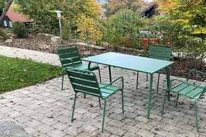 A patio with a green metal table and chairs, surrounded by a brick pathway and trees. - Holiday apartment with 3 bedrooms (Braunlage)