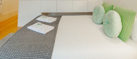 A modern bedroom with a bed, pillows, a bedside table, and a small kitchenette area.