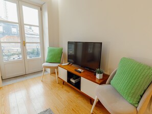 A modern living room with a flat-screen TV, a sofa, a chair, and a small table. - Apartment  by Interhome (Porto)