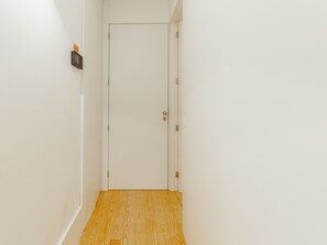 A narrow hallway with a wooden floor, white walls, and a closed door with a keyhole. - Apartment  by Interhome (Porto)