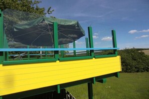 Un espace extérieur aménagé avec des sièges aux couleurs jaune et vert, et un parasol vert offrant de l’ombre.