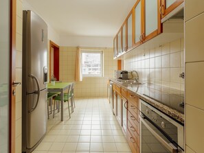 A compact kitchen with a refrigerator, a dining table with chairs, and a window with a view of buildings. - DOWNTOWN DELUXE 3 by VACATIONY by Interhome (Porto)