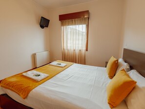 A hotel room with a bed, a television mounted on the wall, a window with curtains, and a radiator. - DOWNTOWN DELUXE 3 by VACATIONY by Interhome (Porto)