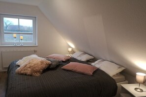 Ein Schlafzimmer mit einem großen Bett, zwei Nachttischen mit Lampen, einem Fenster mit Ausblick und einer Heizung.