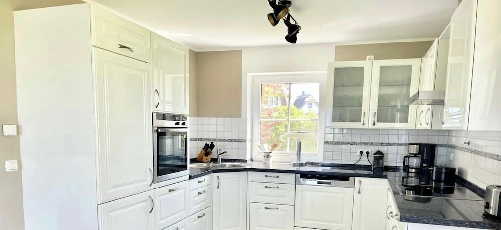 A kitchen with white cabinets, a black countertop, and a window with a view of a house.