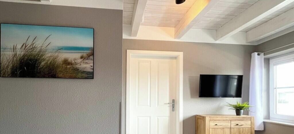 A room with a white door, a flat-screen TV mounted on the wall, and a small wooden cabinet with a plant on top.