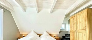 A bedroom with a sloped ceiling, a bed with pillows, bedside lamps, and wooden cabinets. - Holiday home in Dranske with swimming pool (Dranske)
