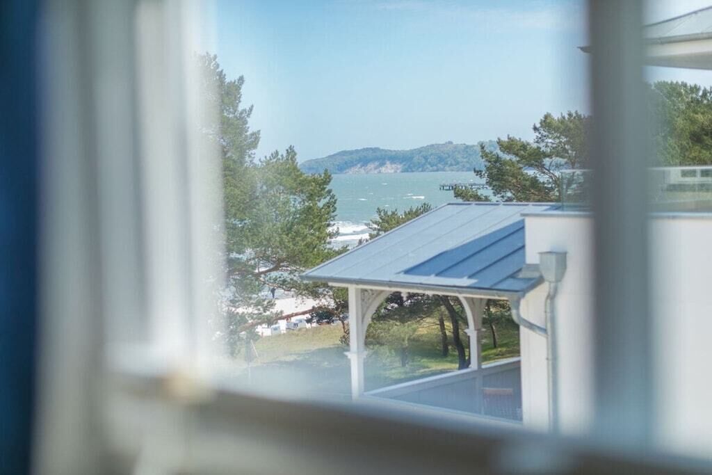 A view through a window of a building with a solar panel roof, a covered outdoor area, and a body of water with boats in the distance.