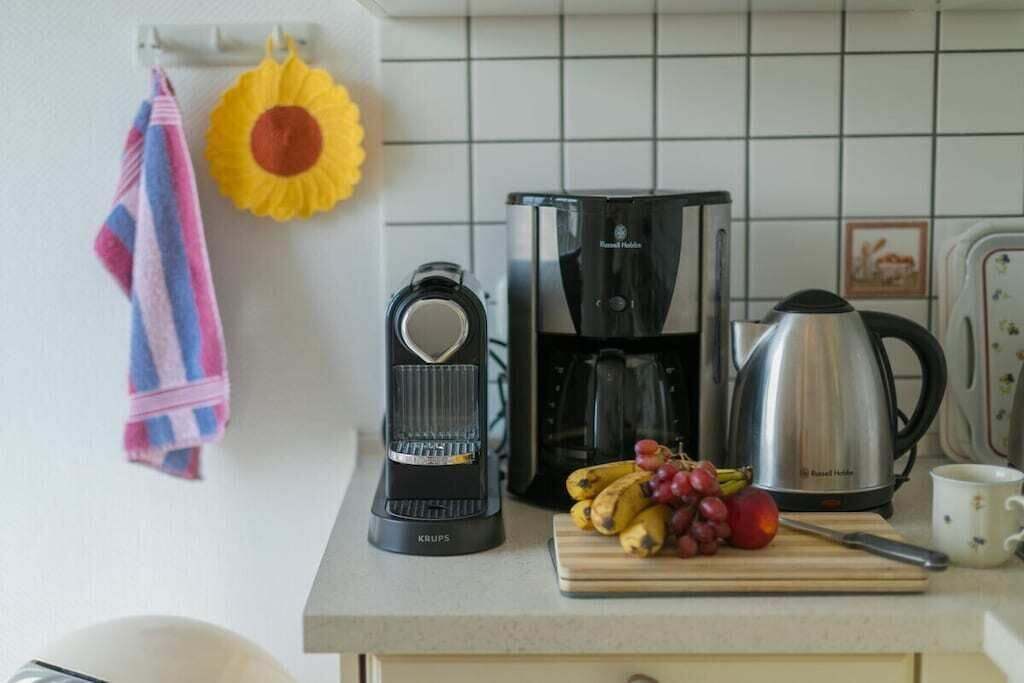 A kitchen with a coffee maker, a kettle, and a cutting board with fruit.