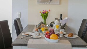Et morgenbord dækket med tallerkener, kopper, en skål med frugt og en kande appelsinjuice.