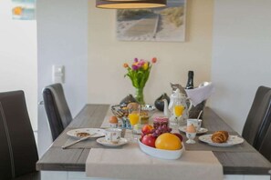 Ein Frühstückstisch mit Tellern, Tassen, einer Obstschale und einem Orangensaftkrug.