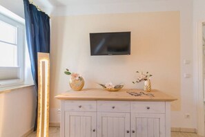 Ein Zimmer mit einem wandmontierten Flachbildfernseher, einer Holzkabine mit Schubladen und zwei Vasen mit Blumen auf der Oberfläche der Kabine.