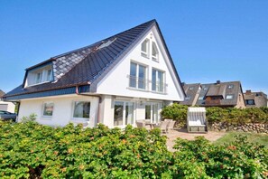 Une maison à deux étages, dotée d’un toit en pente, de grandes fenêtres et d’un balcon.