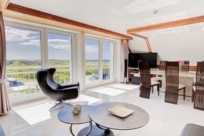 Un salon moderne avec une grande fenêtre, un fauteuil en cuir noir, une table basse ronde et un téléviseur.