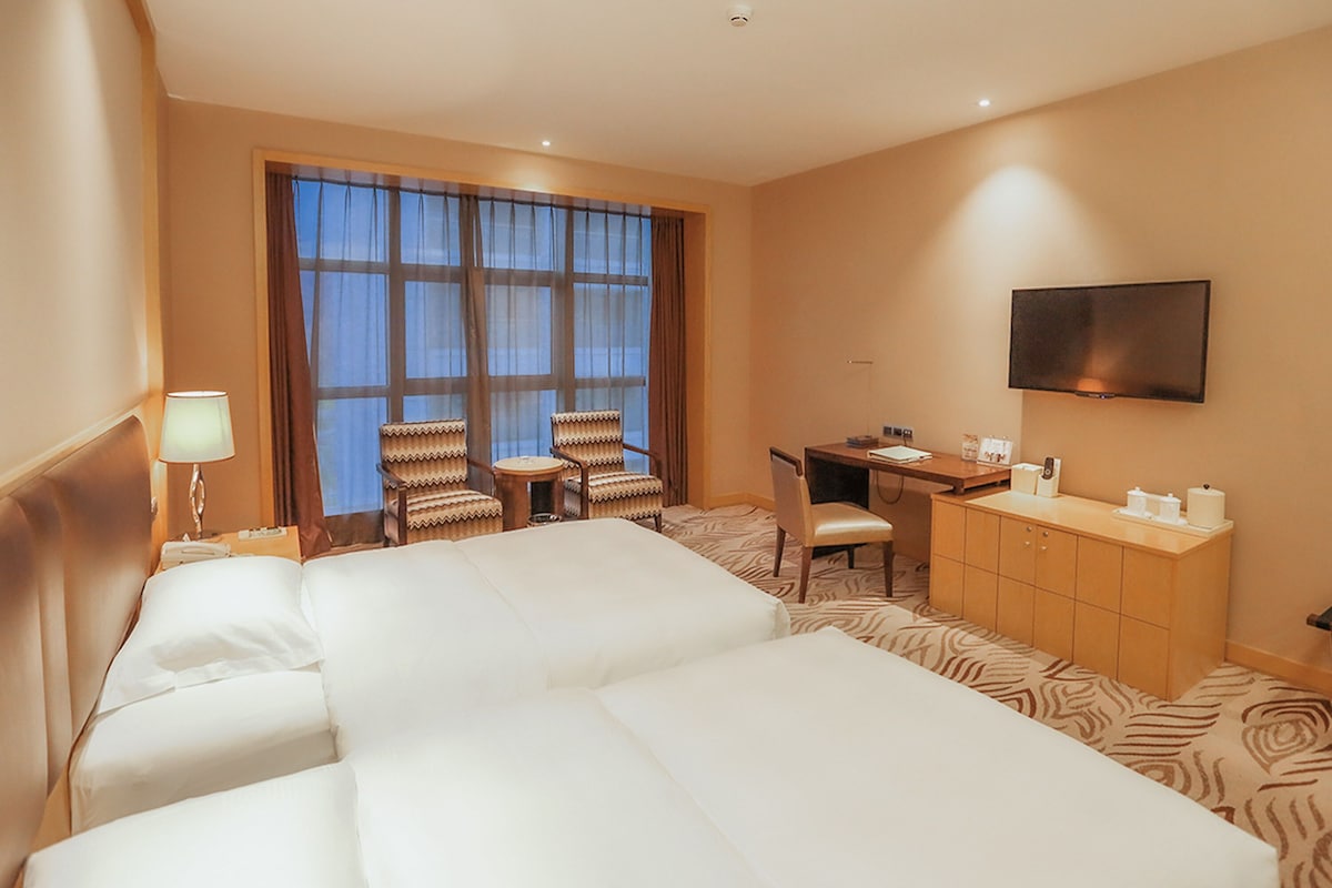 Een hotelkamer met een groot bed, een bureau, twee stoelen, een televisietoestel en een minibar.