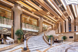 A grand hotel lobby with marble floors, a grand staircase, and a reception desk. - Kingworld Hotel Gui'an (Fuzhou)