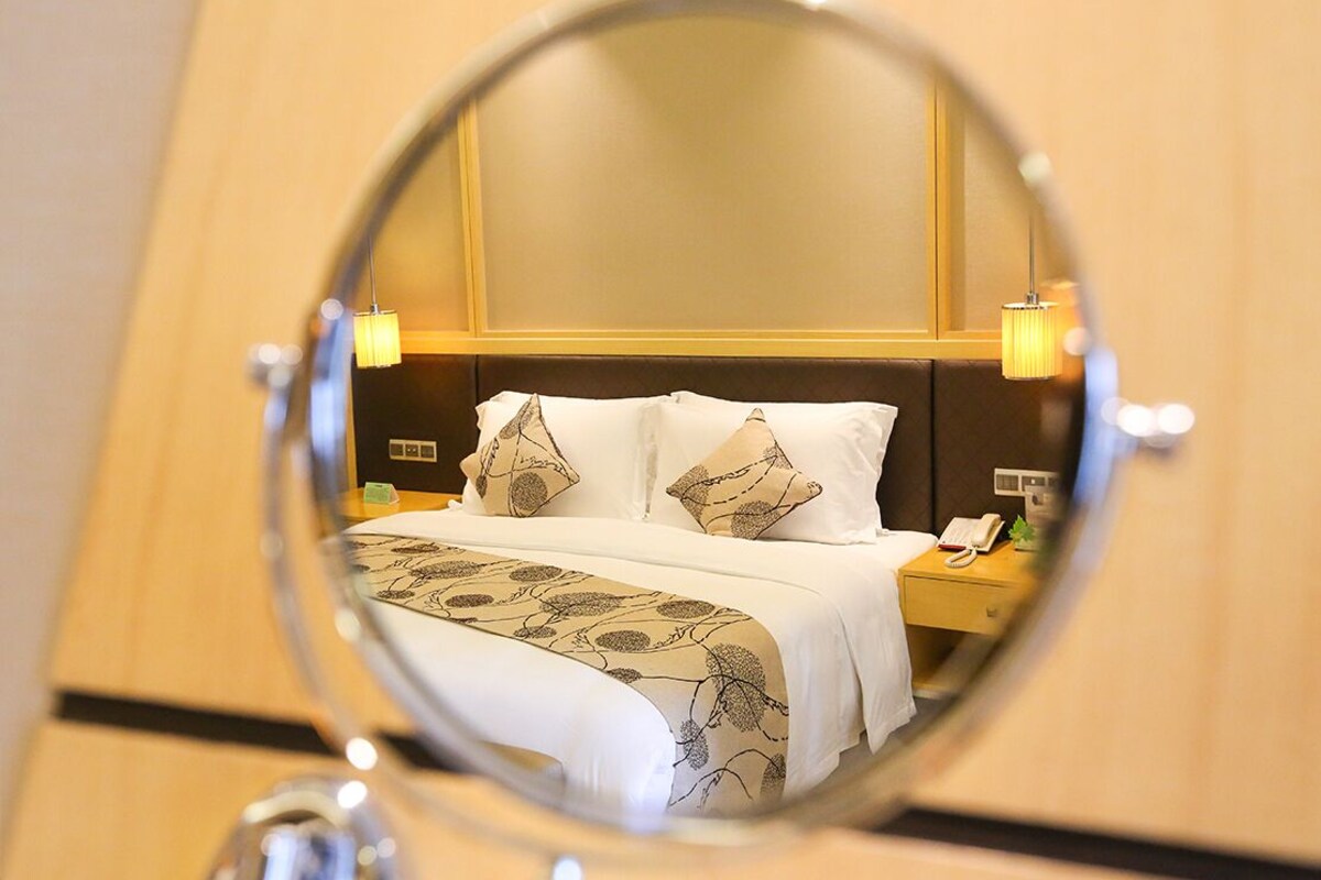 A hotel room with a bed, bedside lamps, a nightstand, and a mirror reflecting the room.