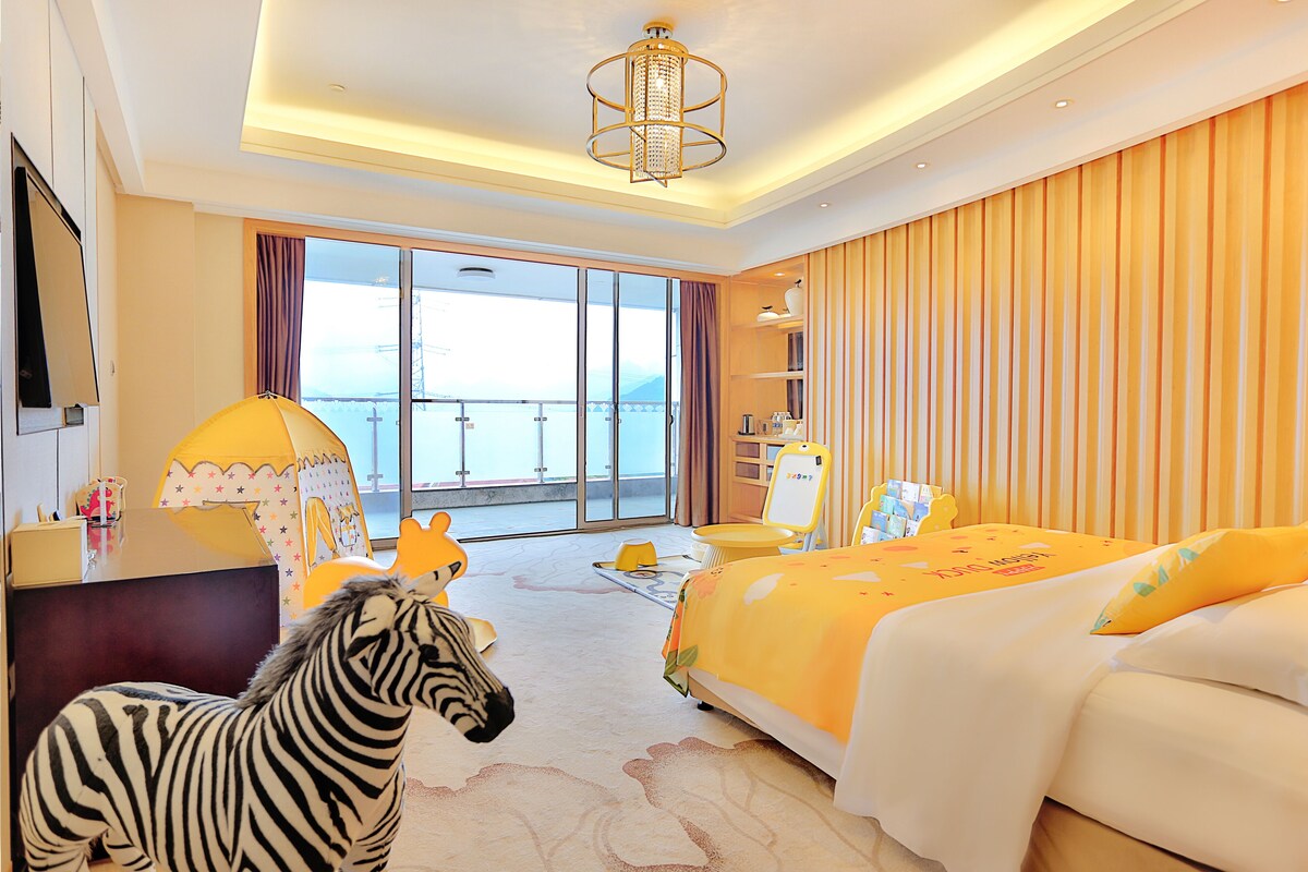 A hotel room with a bed, a desk, a chair, a zebra decoration, and a view of the sea through the window.