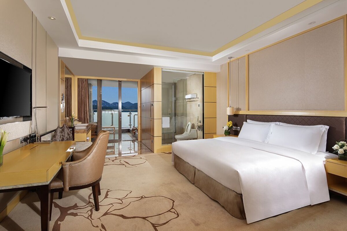 A hotel room with a bed, a desk, a chair, a TV, and a view of the outdoors.