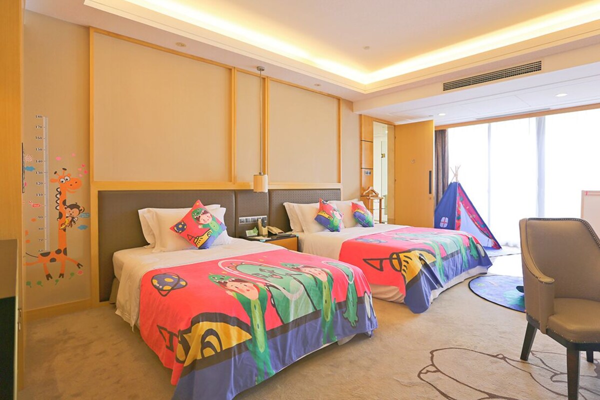 A hotel room with two beds, a chair, and a window.
