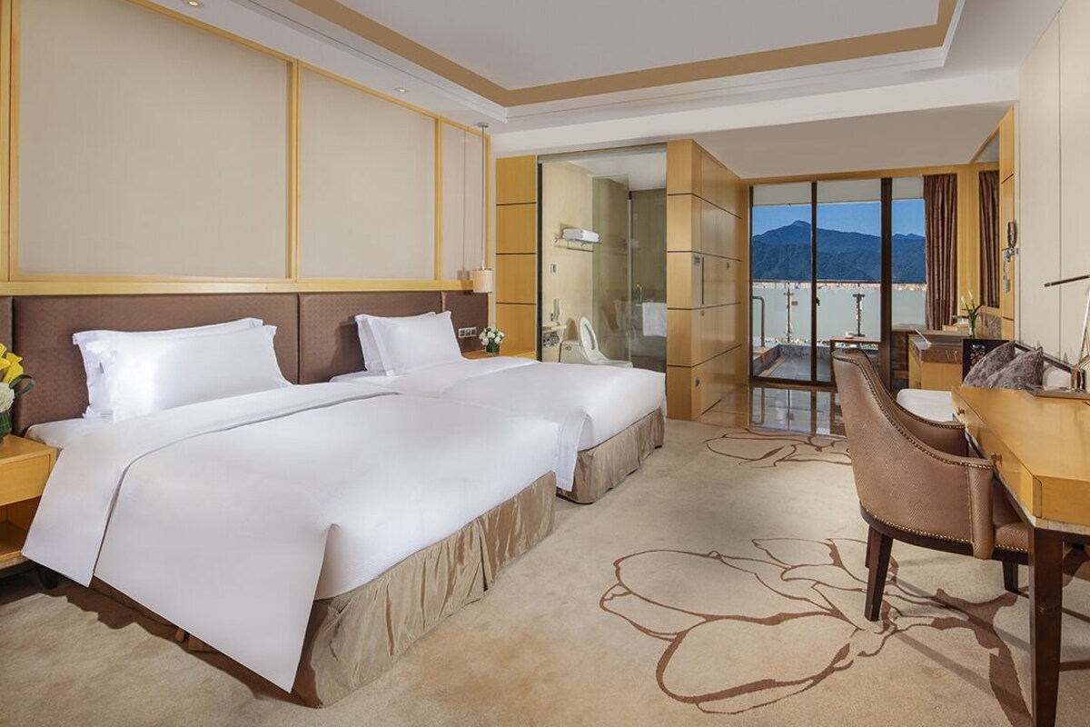 A hotel room with two beds, a desk, and a balcony with a view.