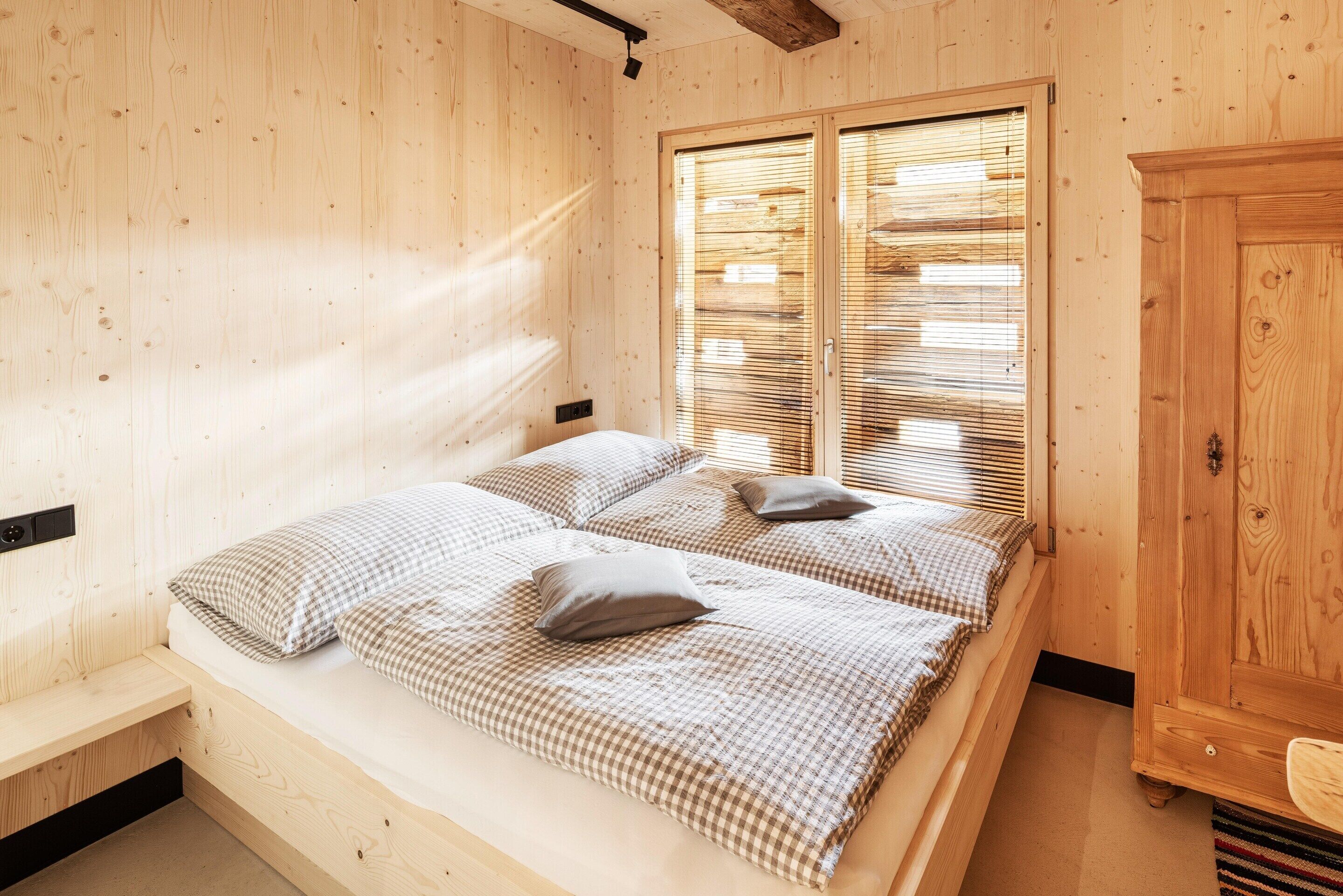 Une pièce en bois avec un lit, une armoire et une fenêtre équipée de stores.
