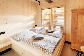 A wooden room with a bed, a wardrobe, and a window with blinds.