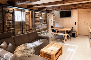 A modern interior with a wooden dining table, a sofa, and a television mounted on the wall. - Raneburg Historic Estate With Sauna (Matrei in Osttirol)