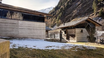 Une cabane rustique au toit en pente, entourée d’un paysage enneigé et dominée par un décor montagneux.