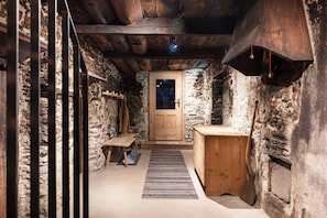 A narrow stone-walled corridor with a wooden door, a bench, and a small wooden table.