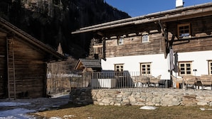 Ein rustikales Holzgebäude mit Steinwand, Sitzgelegenheiten im Freien und Bergblick.