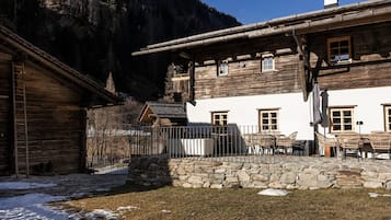 A rustic wooden building with a stone wall, outdoor seating, and a mountain backdrop.