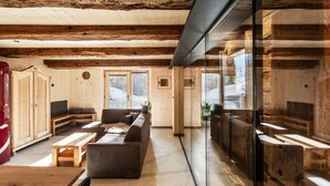 Ein modernes Interieur mit Holzbalkendecke, einer Sofagarnitur, einem Esstisch und einer Glastrennwand.