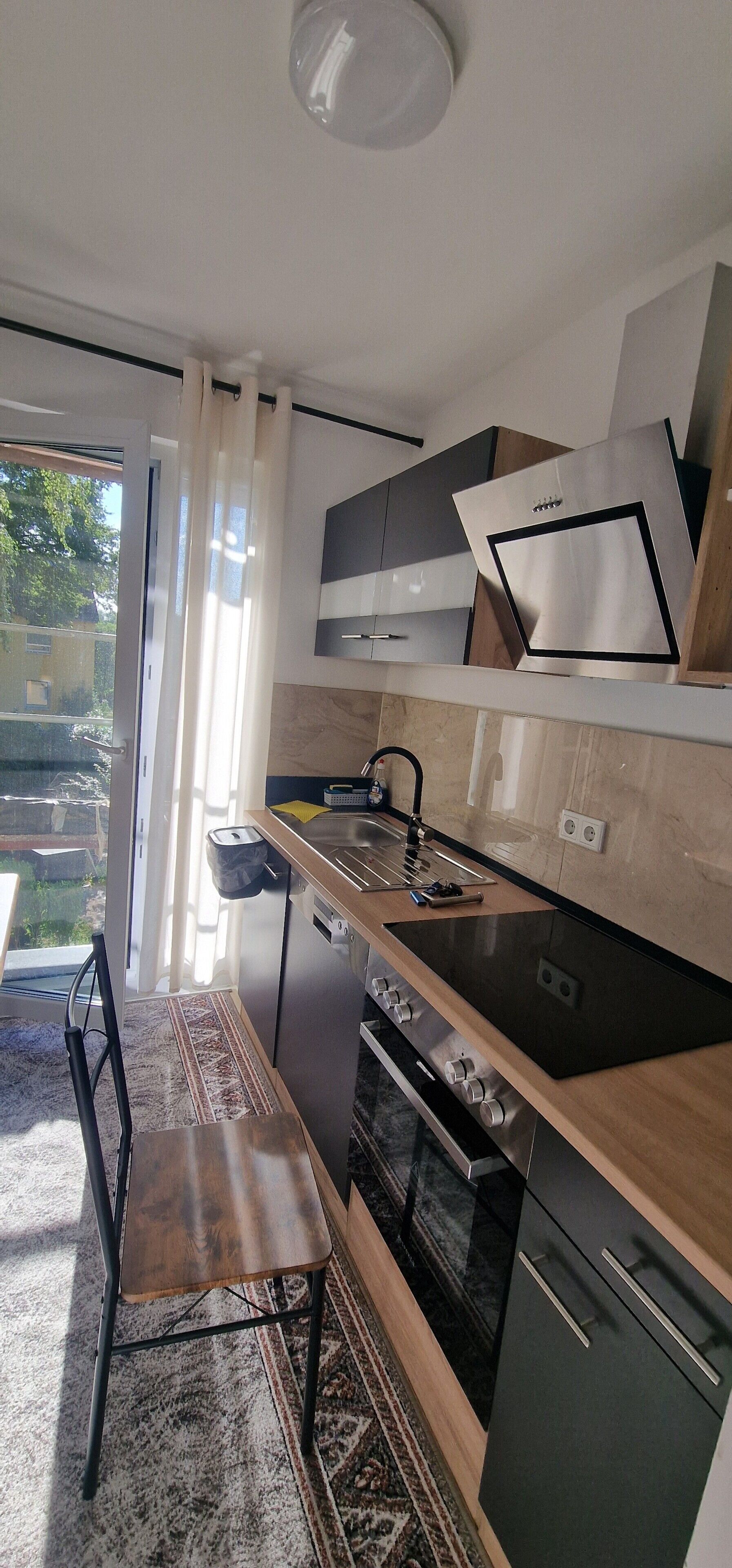 Una cocina moderna con horno empotrado, un lavamanos y una zona de comedor con una silla.