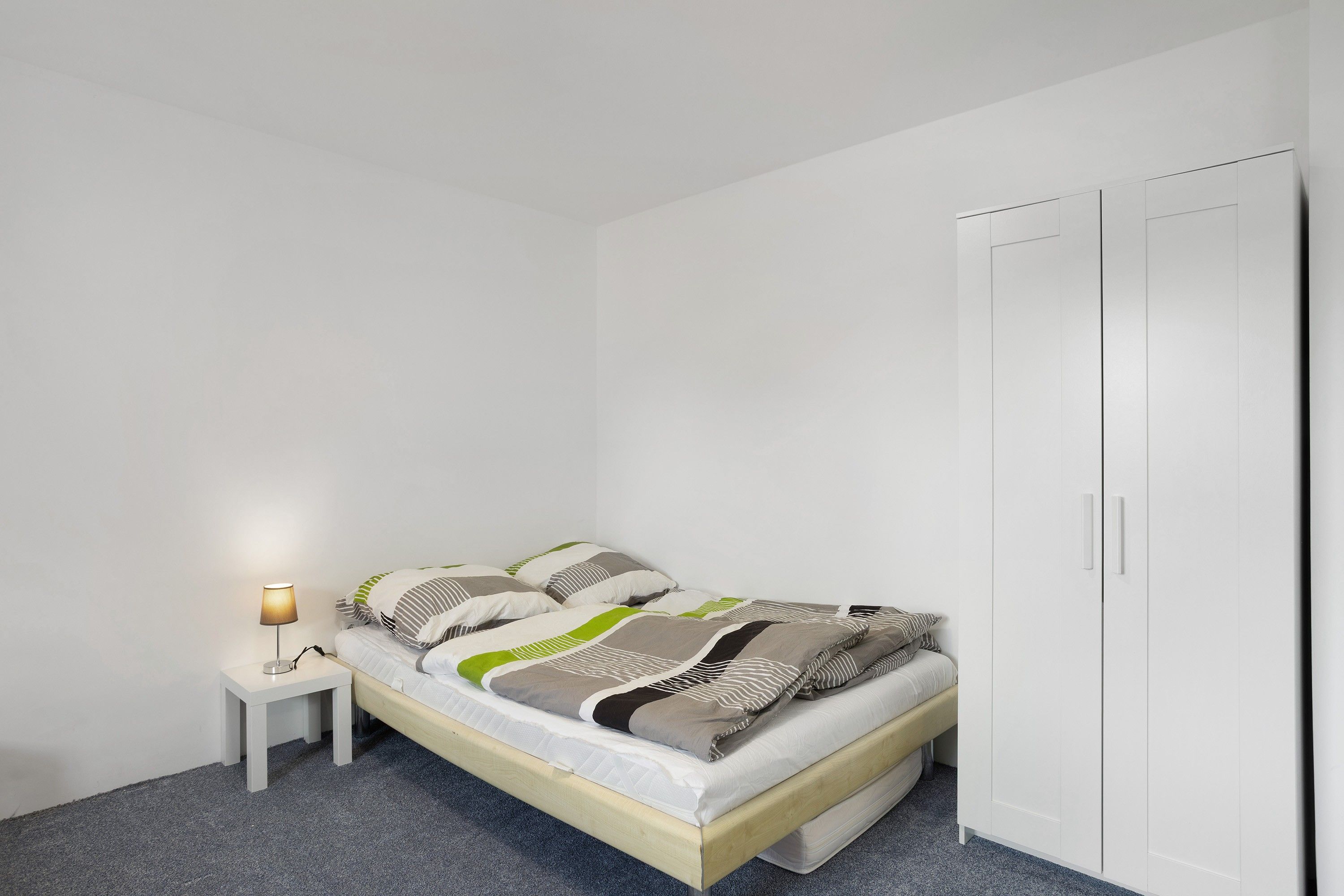 Un dormitorio con cama, mesita de noche con lámpara y armario.