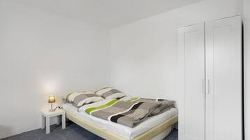 Un dormitorio con cama, mesita de noche con lámpara y armario.