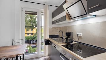 Eine moderne Küche mit Einbauherd, Kaffeemaschine und Blick auf ein gelbes Gebäude durch die Glastür.