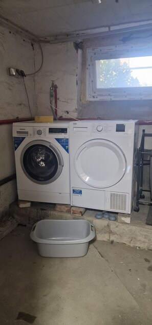 Une machine à laver et un récipient en plastique dans une pièce dotée d’une fenêtre et d’une échelle.