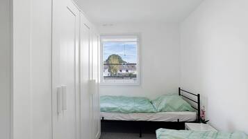A small, narrow room with a single bed, a window, and a wardrobe.