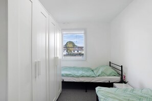 Ein kleiner, schmaler Raum mit einem Einzelbett, einem Fenster und einem Kleiderschrank.