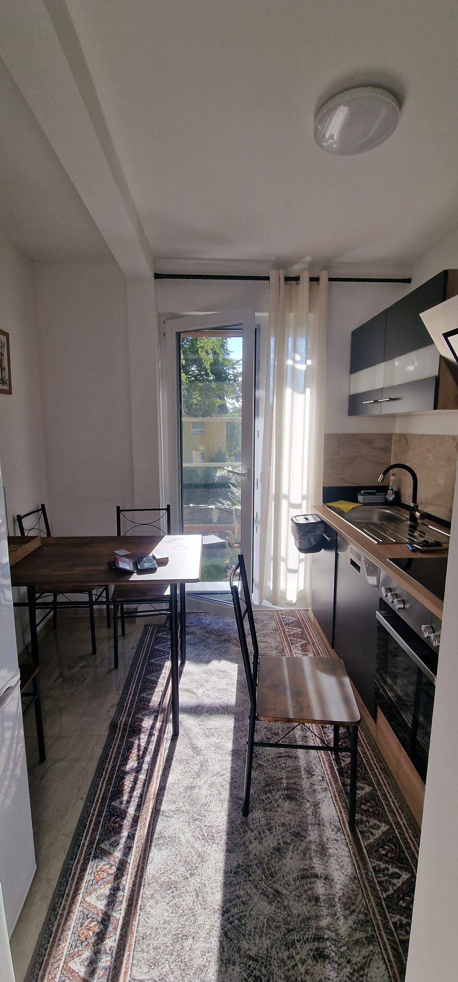 A compact kitchen with a dining area, a built-in oven, and a view through the glass door.
