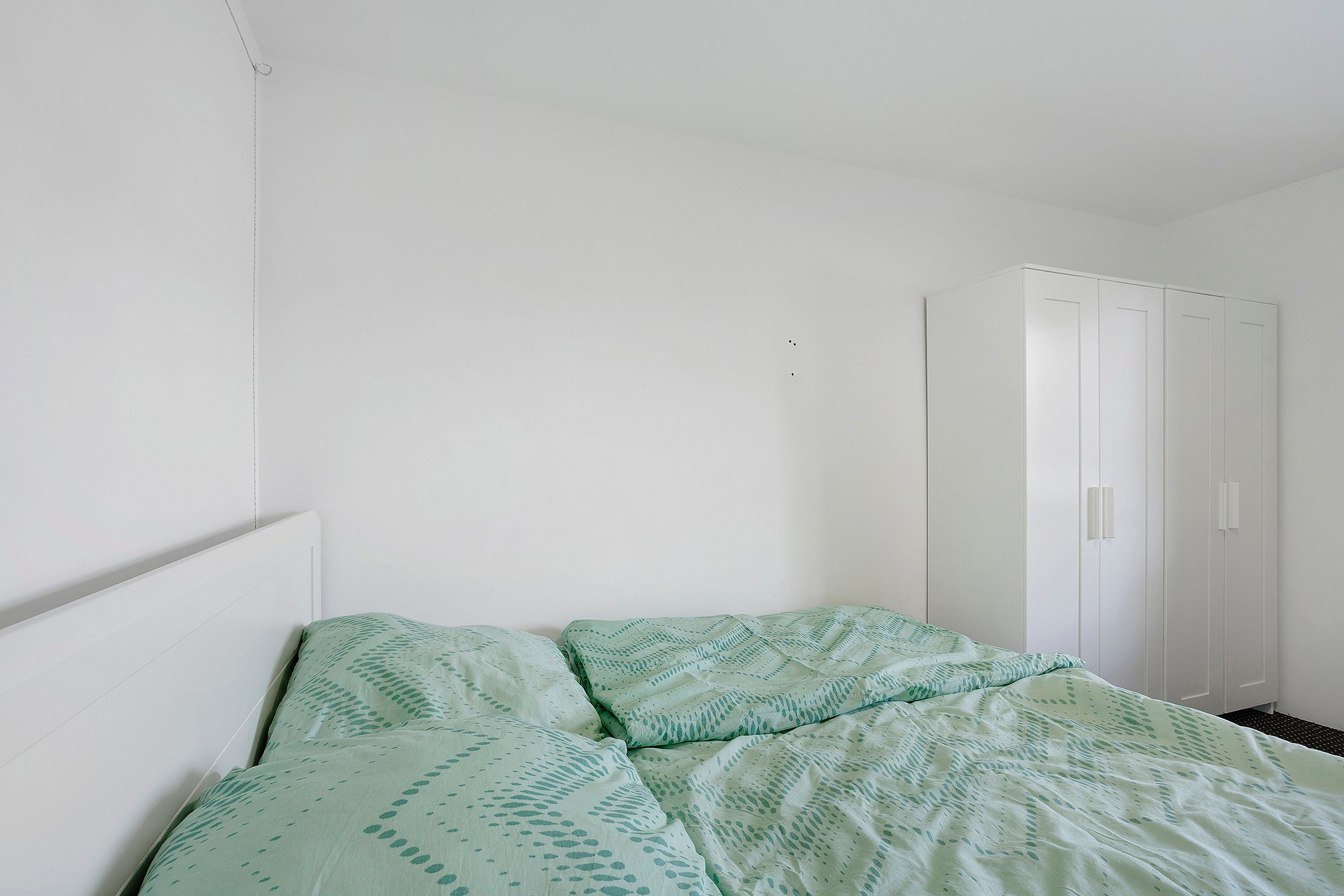 Ein schlichtes Zimmer mit einem Bett, einem Kleiderschrank und einer schlichten Wand.