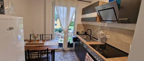 Cocina compacta con horno integrado, un lavamanos y un comedor con mesa y sillas.