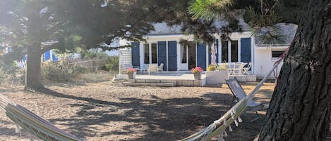 Una casa con porche cubierto, mobiliario exterior y una hamaca.