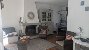 A cozy living room with a fireplace, wicker furniture, and a dining area with a table and chairs. - Family villa by the sea (La Turballe)
