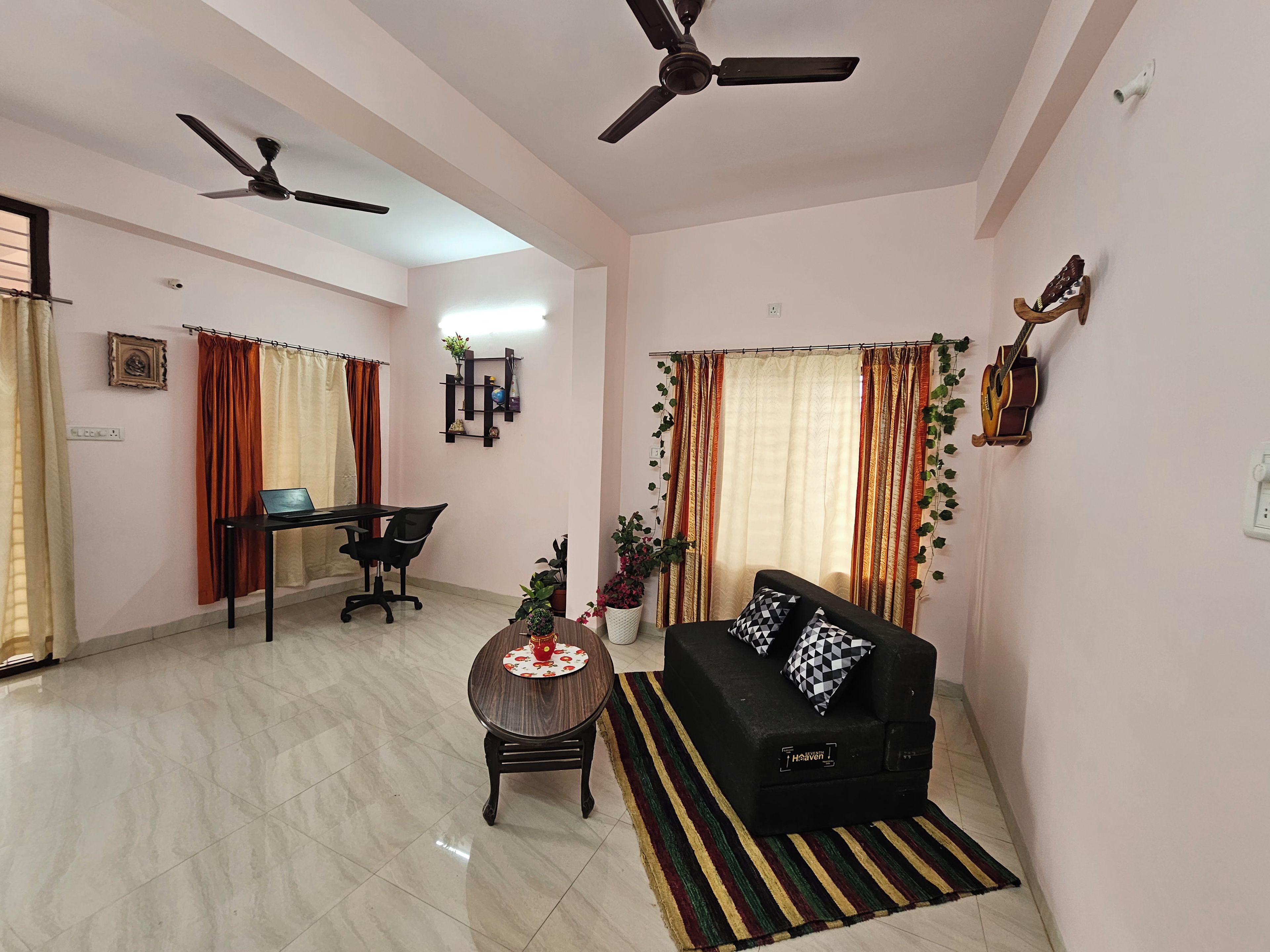 A living room with a sofa, a dining table with chairs, a ceiling fan, and a wall-mounted guitar.